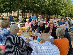 Vereinsmitglieder sitzen vor dem münsteraner Schloss an einem reichlich gedeckten Frühstückstisch und unterhalten sich.