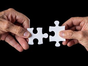 Zwei weiße Puzzlestücke werden von Händen gehalten, nicht sicher, ob sie ineinander passen..