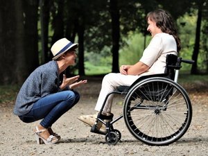 Rollstuhlfahrerin und Begleitperson lachen in der Natur