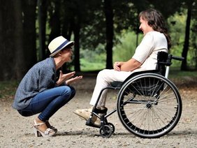 Rollstuhlfahrerin und Begleitperson lachen in der Natur